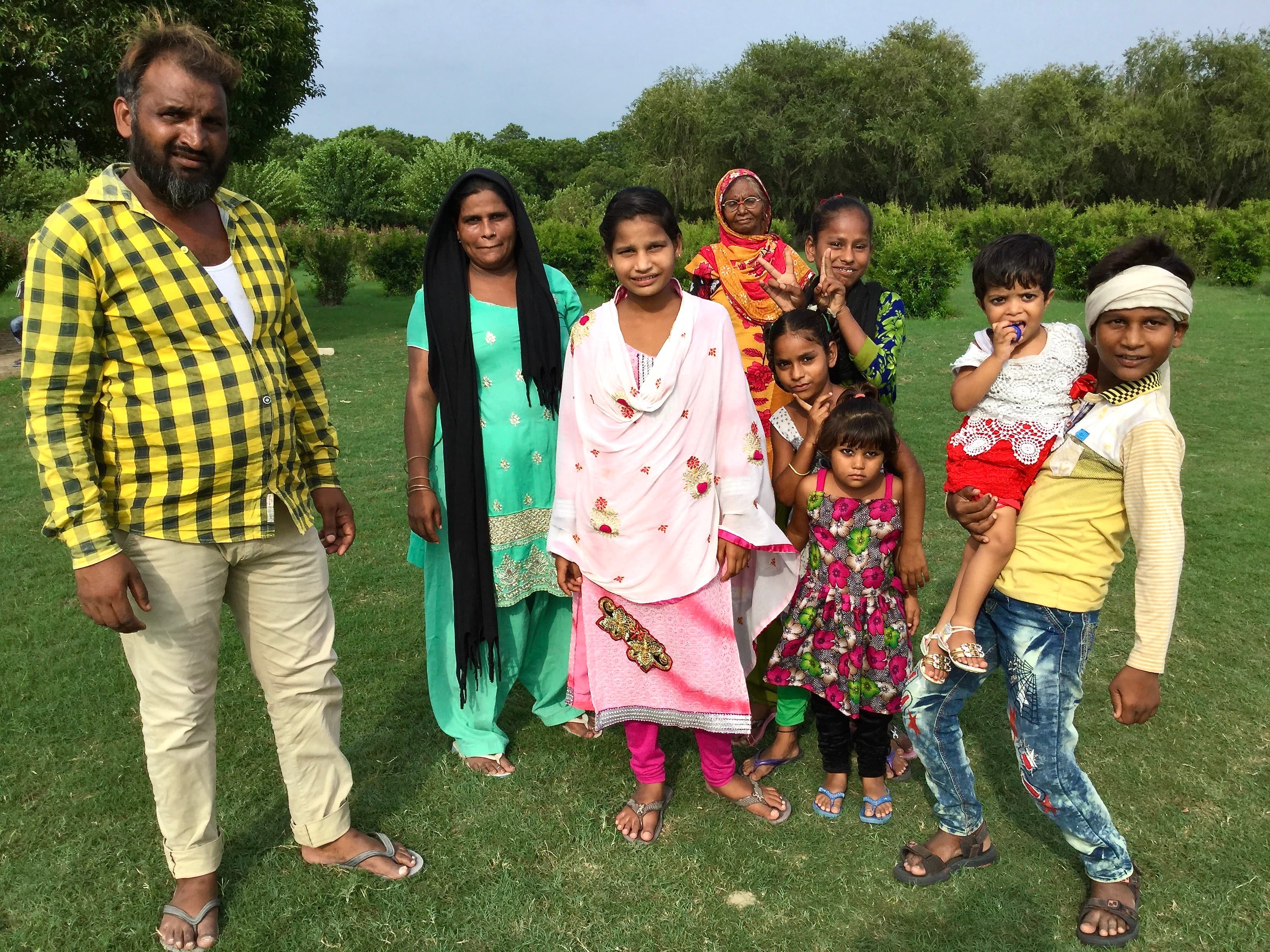 A group of nine people in colorful South Asian clothing pose on a green lawn.
