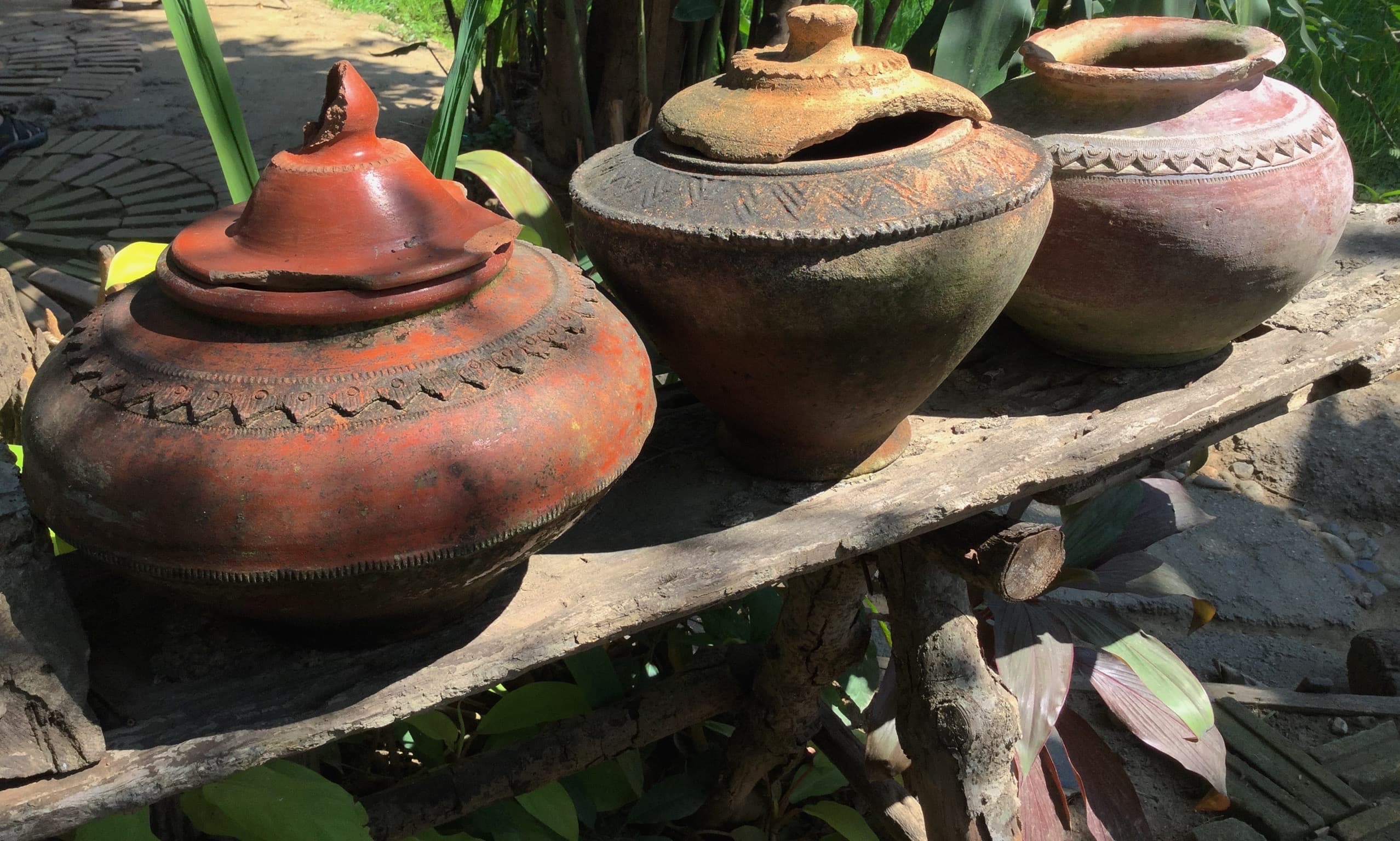 Three weathered clay pots with ornate patterns sit on a rustic wooden bench outdoors.