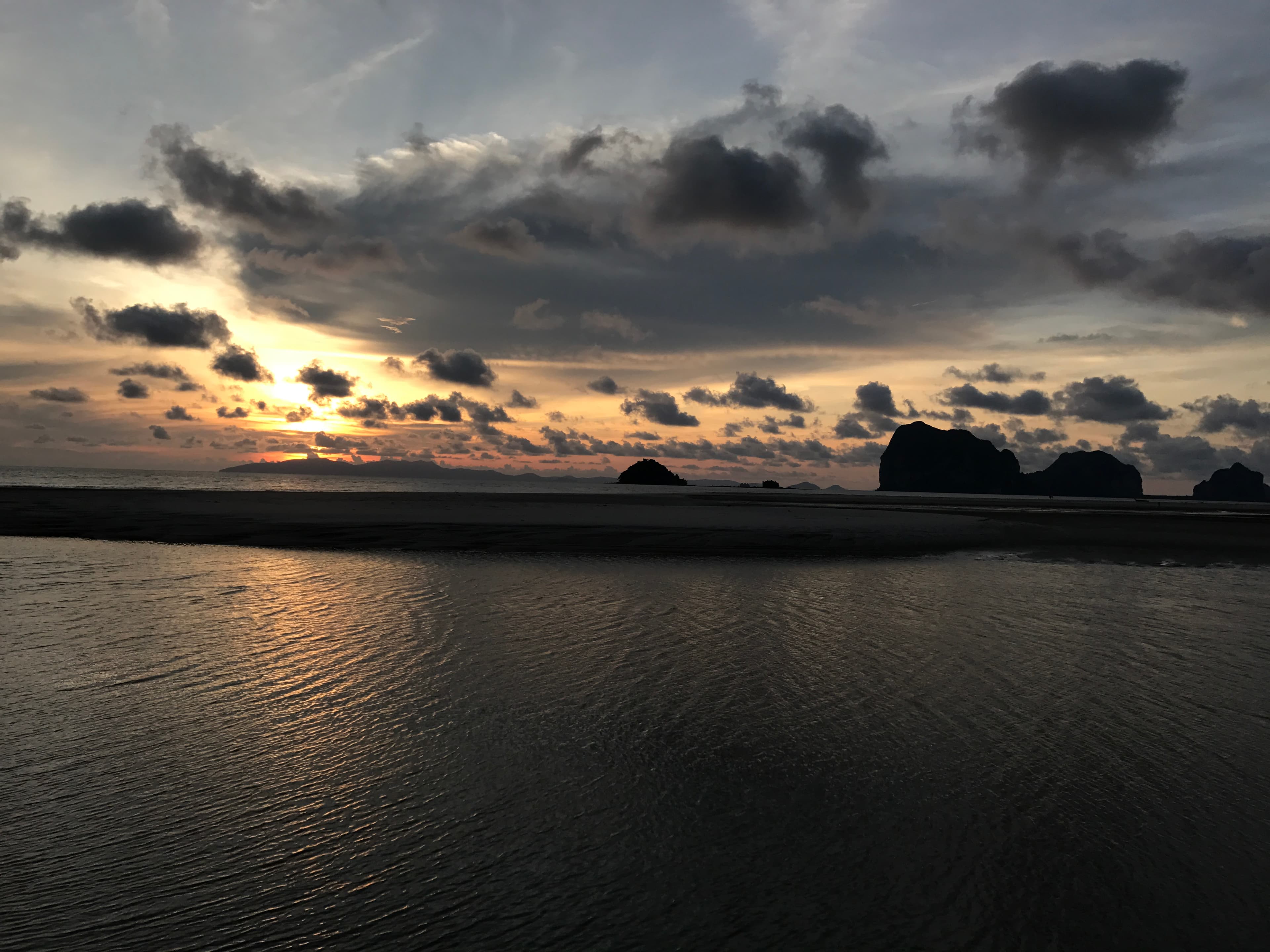 Golden sunset reflecting on rippled water with dark island silhouettes under a dramatic cloudy sky.